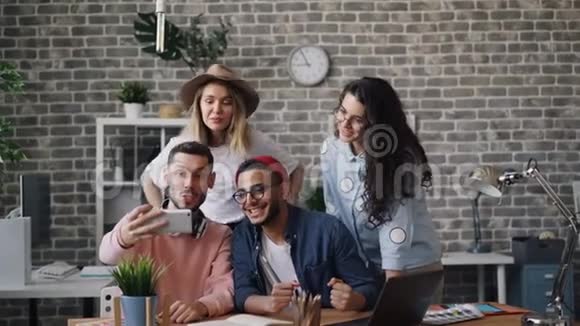 一群女孩和男人在办公室里用智能手机摄像头自拍视频的预览图
