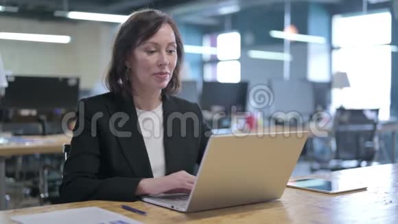 快乐的中年女商人在办公室的笔记本电脑上聊天视频的预览图
