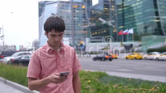 年轻的帅哥使用智能手机在大工业大厦旁行走视频的预览图