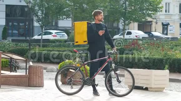 一个带着黄色包和自行车的快递员正在电话里寻找客户的地址年轻的送货员视频的预览图