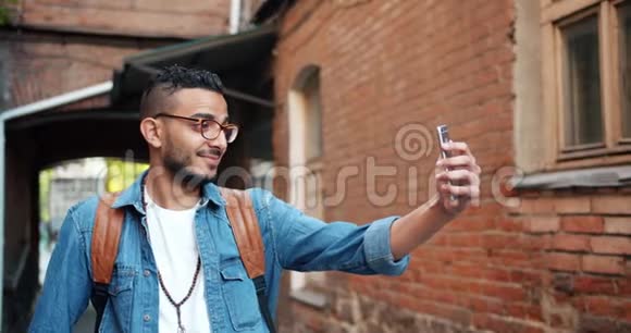 活泼开朗的阿拉伯男人在户外用智能手机自拍视频的预览图