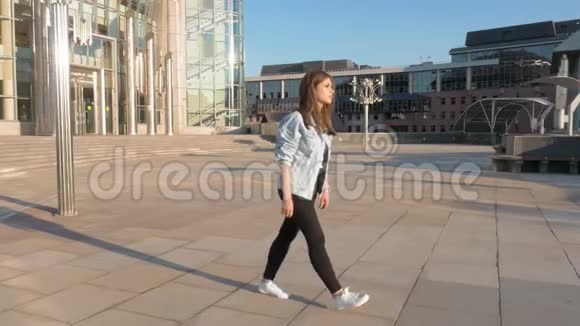 年轻的棕色头发的女人穿着蓝色夹克和黑色裤子走在空荡荡的街道上视频的预览图