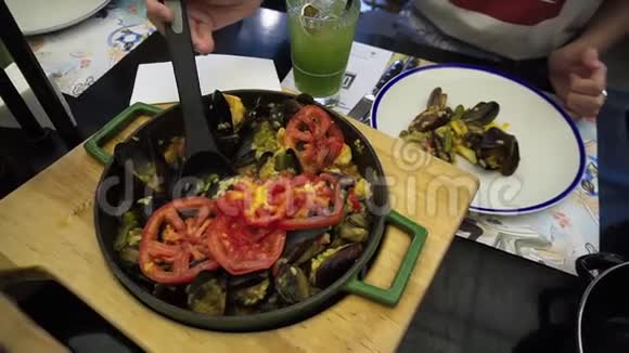 一个女孩在一盘传统的西班牙菜肴上倒入海鲜和蔬菜的海鲜饭视频的预览图