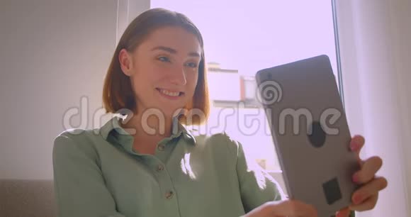 年轻性感女学生坐在客厅的沙发上坐在平板电脑上的视频聊天的肖像视频的预览图