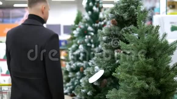 为圣诞节和新年做好准备男人在商店里选择人造圣诞树和圣诞树装饰品视频的预览图