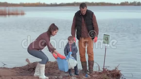 生态灾难男女志愿者带着男童在附近海滩收集塑料和聚乙烯垃圾视频的预览图
