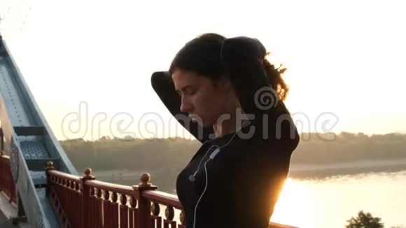 穿黑色衣服的运动女孩准备训练跑步者在黎明时把头发扎成马尾太阳阳光视频的预览图