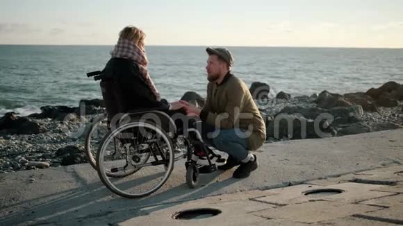 男人牵着轮椅上生病的年轻女子的手和她说话视频的预览图
