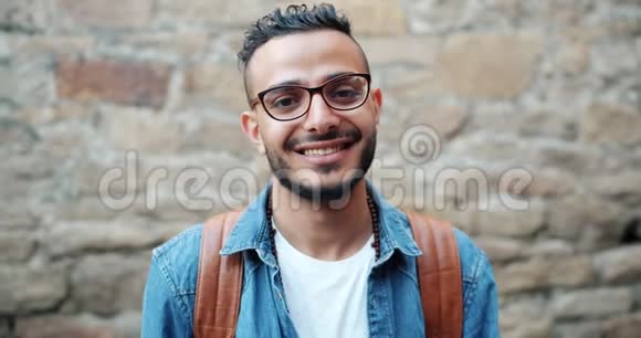 有魅力的年轻阿拉伯人微笑着看砖墙附近的摄像机的画像视频的预览图