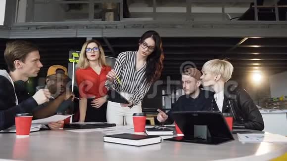 创意女性团队领导站在桌子旁边指导年轻创意团队在办公室开会视频的预览图