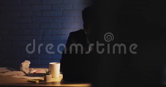 办公室工作人员在深夜工作在笔记本电脑上他打哈欠喝咖啡只有一个商人视频的预览图