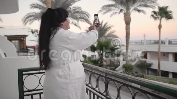 微笑的白种人高级妇女在智能手机上自拍照片应该在酒店的露台上白色的视频的预览图