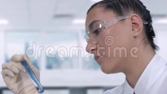 一位女科学家正在试管中进行一种蓝色液体的实验室测试当时她正坐在科学桌旁视频的预览图