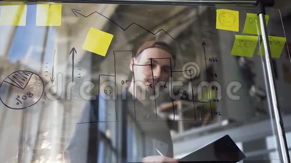 白种人年轻商人穿着休闲服装在计算和编制报告时使用带有图表的玻璃板视频的预览图
