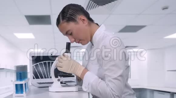 一位女实验室技术人员坐在化学实验室笔记本电脑旁的桌子旁在一个实验室里看生物样本视频的预览图