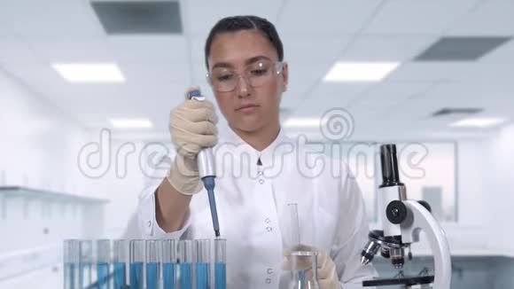 一位女科学家坐在一张桌子旁用微型吸管和试管检查一个蓝色液体样本视频的预览图