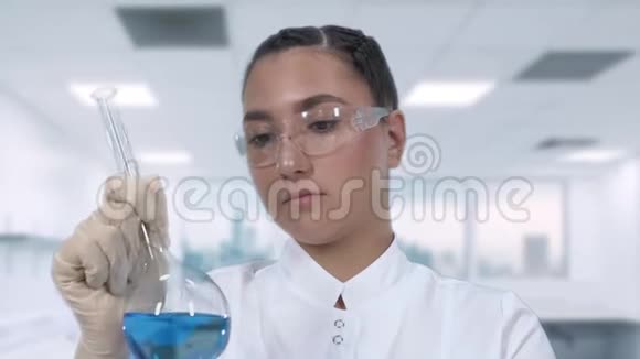 一位女实验室技术人员在玻璃瓶中检查一种蓝色液体并在一个科学实验室进行临床研究关闭视频的预览图