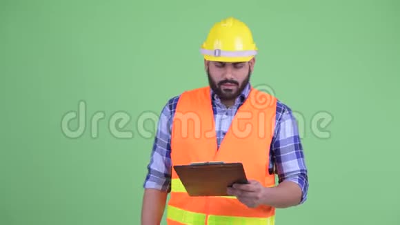 快乐的年轻超重长胡子的印度工人一边拿着夹子一边说话视频的预览图