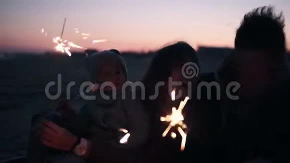 在海滩上一家三口幸福微笑的人坐在篝火旁闪闪发光视频的预览图