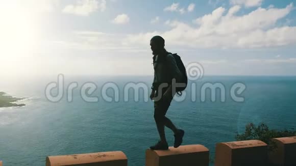年轻自信的留着胡须的徒步旅行者的剪影背包行走在加那利岛上高高的公路边缘视频的预览图
