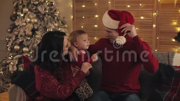 在舒适的家中度假背景下爸爸妈妈和可爱的小男孩坐在沙发上靠近圣诞树视频的预览图