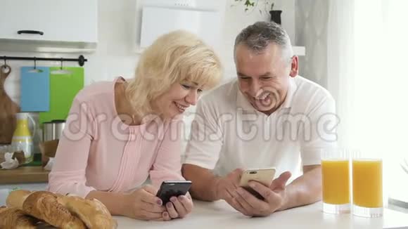 高级家庭夫妇在厨房早餐时享受数字技术视频的预览图