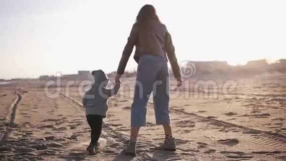 穿着暖和的衣服的有趣的妈妈和宝宝在海边的沙滩上跳舞跑步和玩太阳视频的预览图