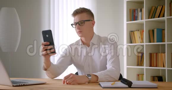 年轻英俊的白种人商人戴着眼镜在手机前摆姿势自拍的特写照片视频的预览图