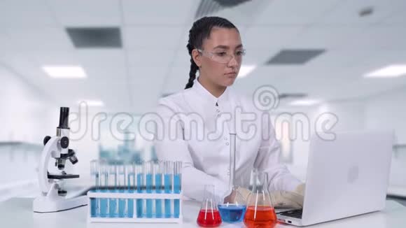 一位女科学家在化学实验室里坐在一张白色的桌子上把临床试验数据写到笔记本电脑上视频的预览图