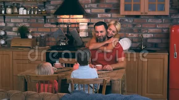 爸爸妈妈和两个孩子聚集在厨房的餐桌上吃晚饭视频的预览图