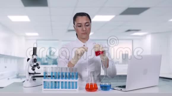 一位女科学家将一瓶红色液体倒入试管中坐在白色的旁边进行临床试验视频的预览图