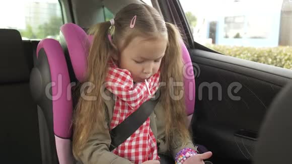 小女孩在车里用智能手机可爱的少女在智能手机上玩而骑在后座上开车视频的预览图