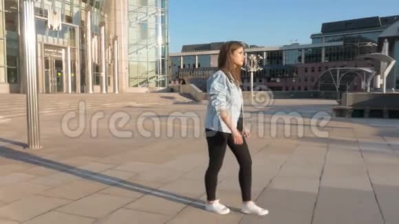 年轻的棕色头发的女人穿着蓝色夹克和黑色裤子走在空荡荡的街道上视频的预览图