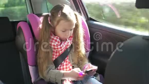 小女孩在车里用智能手机可爱的少女在智能手机上玩而骑在后座上开车视频的预览图