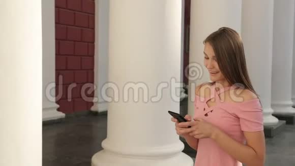年轻女孩拿着智能手机穿着带高跟鞋的粉红色连衣裙高兴和跳跃视频的预览图