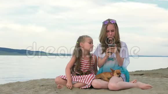 两个十几岁的孩子坐在海滩上打电话视频的预览图
