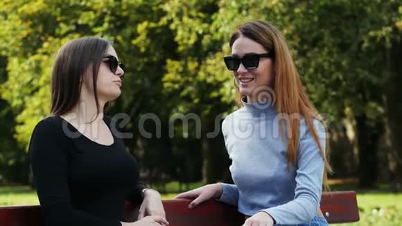 在阳光明媚的一天两个快乐的女人在公园里坐在长凳上聊天聊天视频的预览图