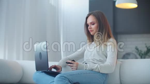 漂亮的年轻女子坐在客厅里一边用手提电脑工作一边出示信用卡视频的预览图