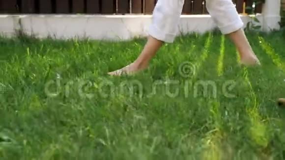 苗条的妈妈和小男孩的腿赤脚走在绿色的草坪上视频的预览图