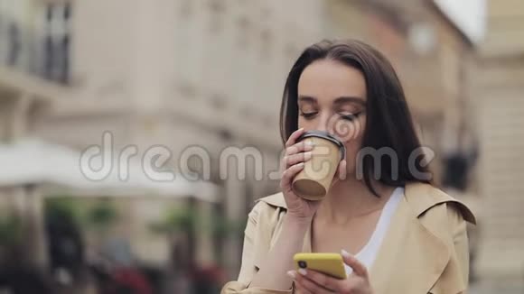 年轻貌美的女孩用智能手机和微笑拿着纸杯喝咖啡站在老人面前的画像视频的预览图