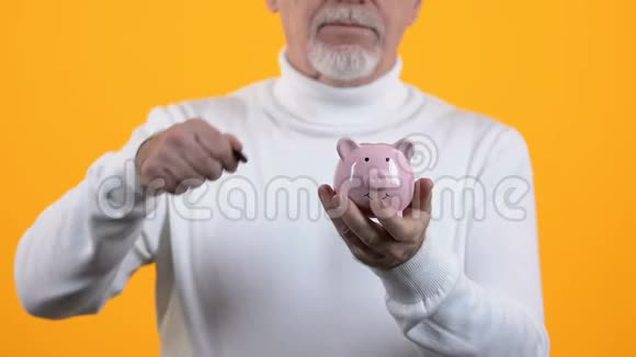 高级绅士把硬币放在橙色背景的储蓄罐上养老基金视频的预览图