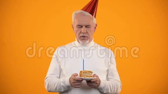 孤独的老年男性在生日蛋糕上吹蜡烛悲伤地看着相机视频的预览图