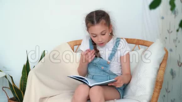 小女孩坐在扶手椅上拿着书在卧室里看书慢动作视频的预览图