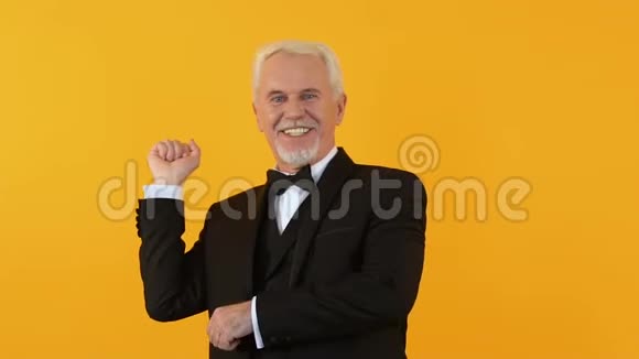 快乐英俊的退休老人在橙色背景上跳舞在镜头上微笑有趣视频的预览图