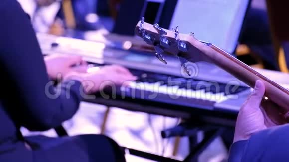 低音吉他手和钢琴家特写男手在女手的背景下握着五弦吉他的弦视频的预览图