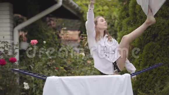 快乐有趣可爱的年轻女人在后院唱歌跳舞享受节奏同时做家务视频的预览图