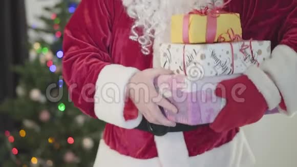 穿着圣诞老人服装的老白种人在新年树前给相机送礼物男子手持礼品盒视频的预览图