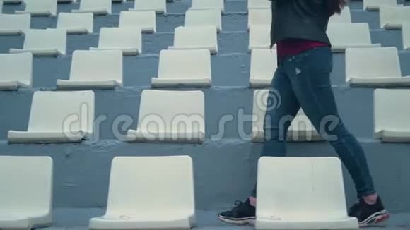 一个穿牛仔裤和运动鞋的女孩的腿在体育场的座位上视频的预览图