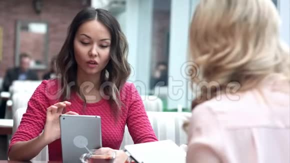 两个女人坐在乡村咖啡馆里看着数码平板电脑上的照片视频的预览图