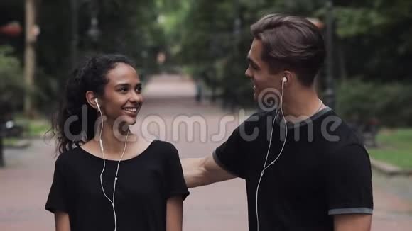 漂亮的音乐女孩和年轻人戴着耳机说话的人在公园慢动作中显示拇指向上和微笑视频的预览图